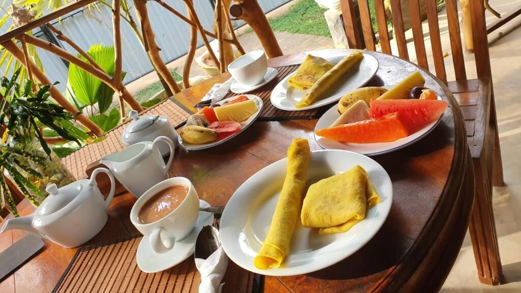A table set with a teapot, cups, plates of food including crepes, and a bowl of soup.