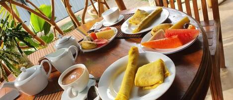 A table set with a teapot, cups, plates of food including crepes, and a bowl of soup.