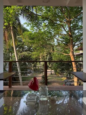 Una mesa de vidrio con vistas a un jardín exuberante, un objeto rojo sobre la mesa y una baranda de metal.