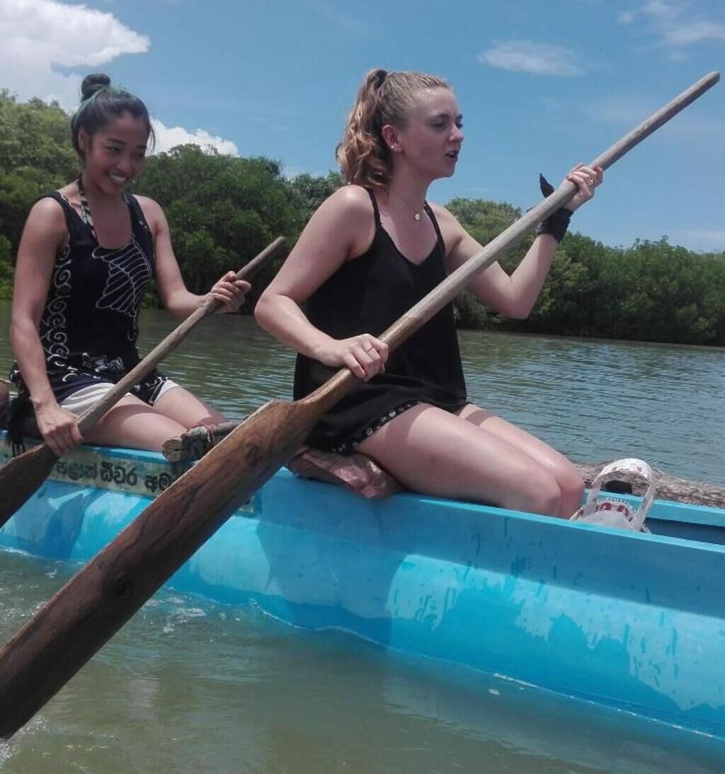Two people rowing a blue boat with wooden oars.