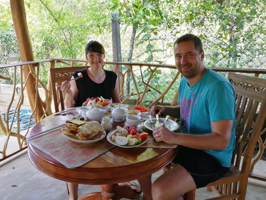 Two people seated at an outdoor wooden table with a variety of food items and drinks.