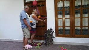 Un homme et une femme se tiennent devant une porte en bois, avec un pot de fleurs placé à leurs côtés.