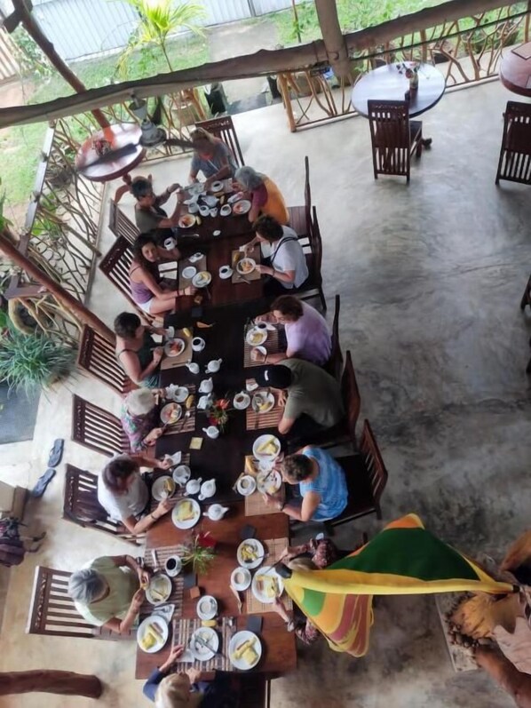 Un espacio de comedor al aire libre cubierto con varias mesas y sillas, rodeado de plantas y una cerca de metal.