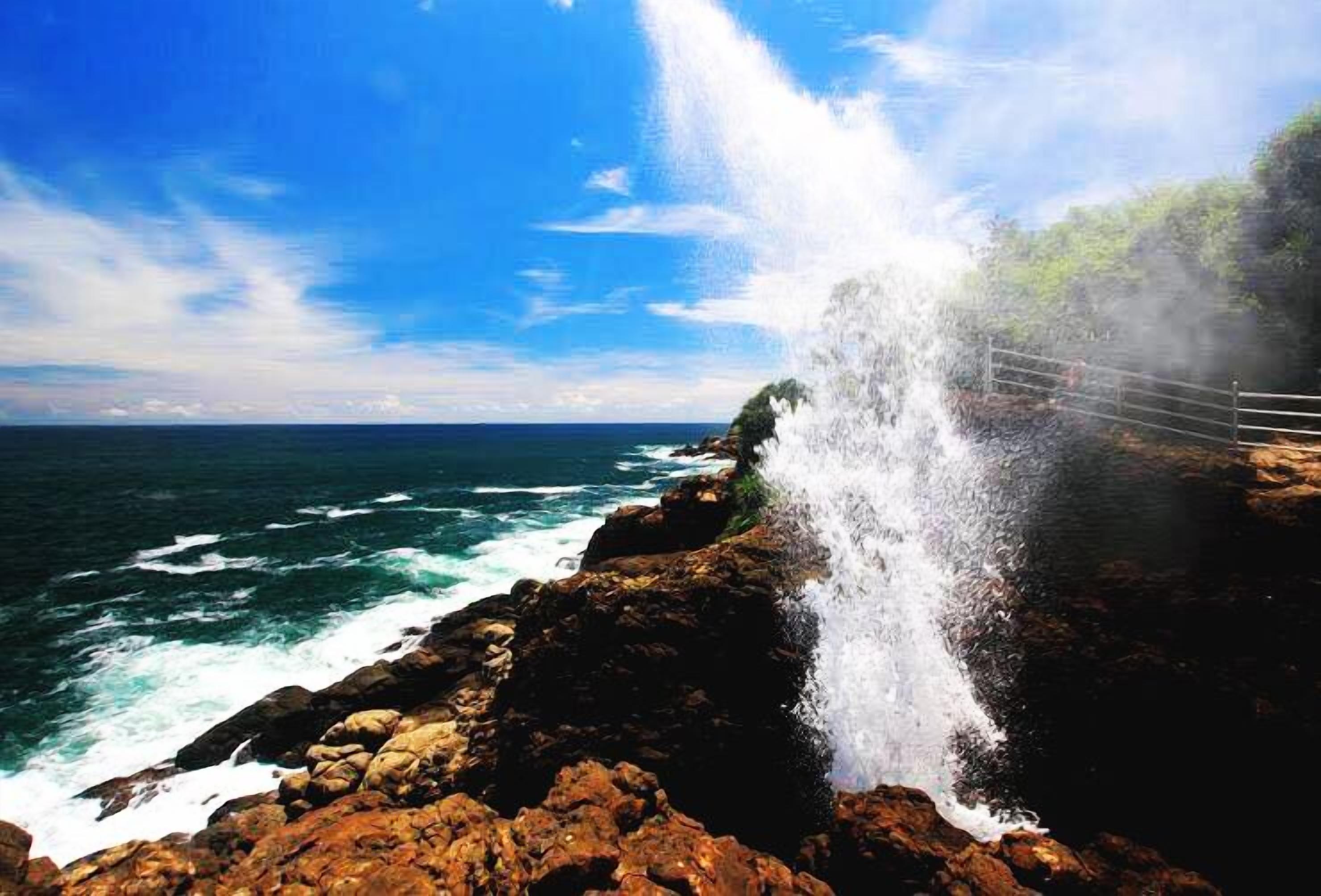 A coastal scene with a waterfall, rocky terrain, and a clear view of the ocean.