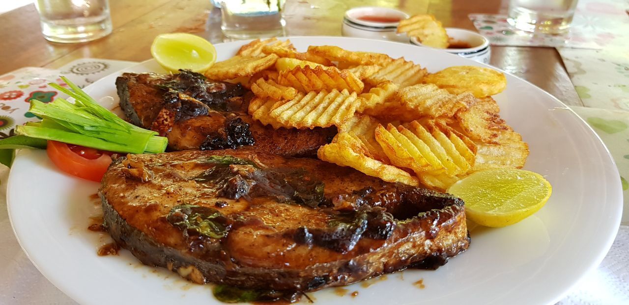 Une assiette de poisson grillé, de frites et une tranche de citron sur une table.