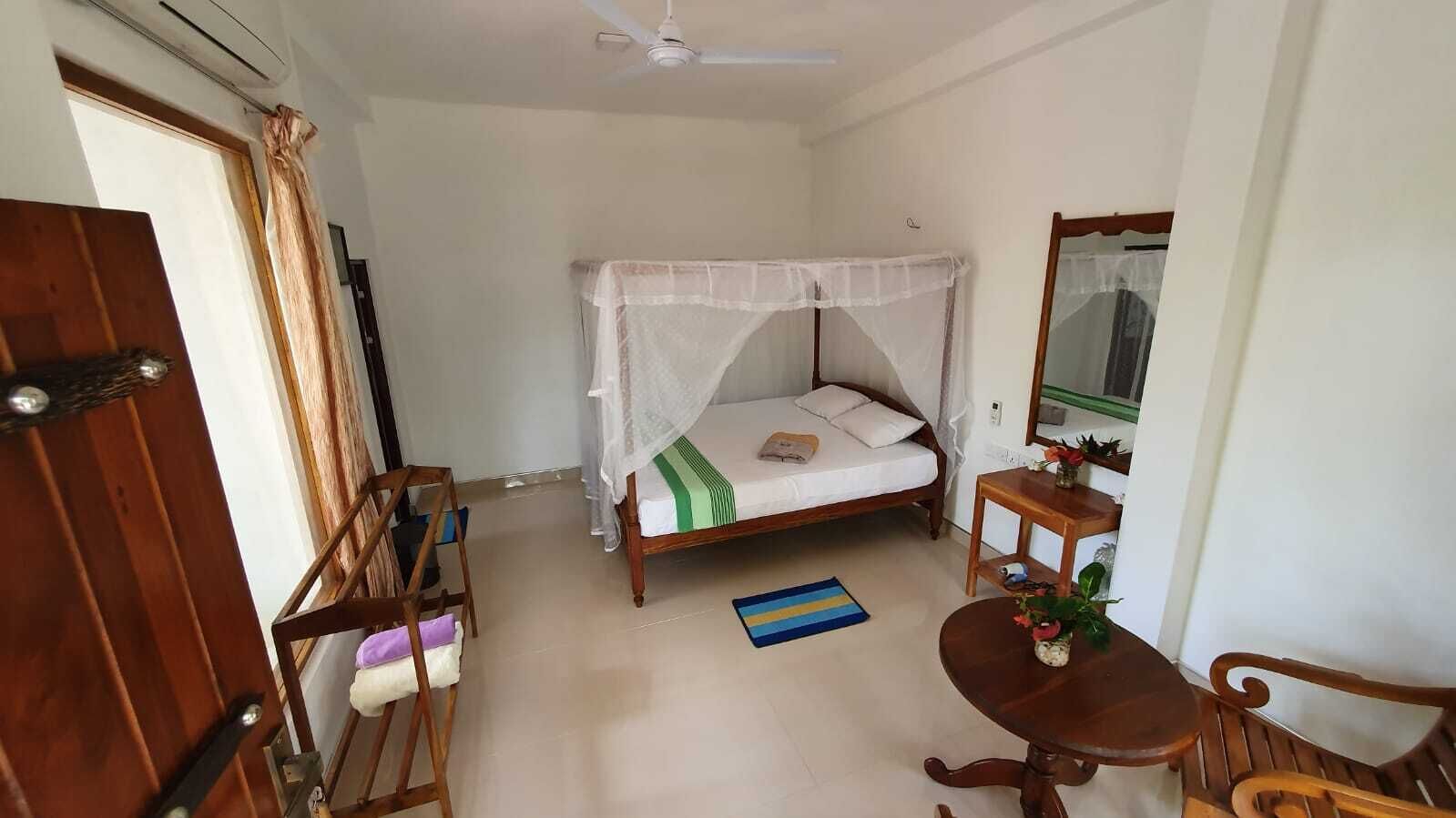 A bedroom with a bed, bedside table, chair, and a small table with a plant.