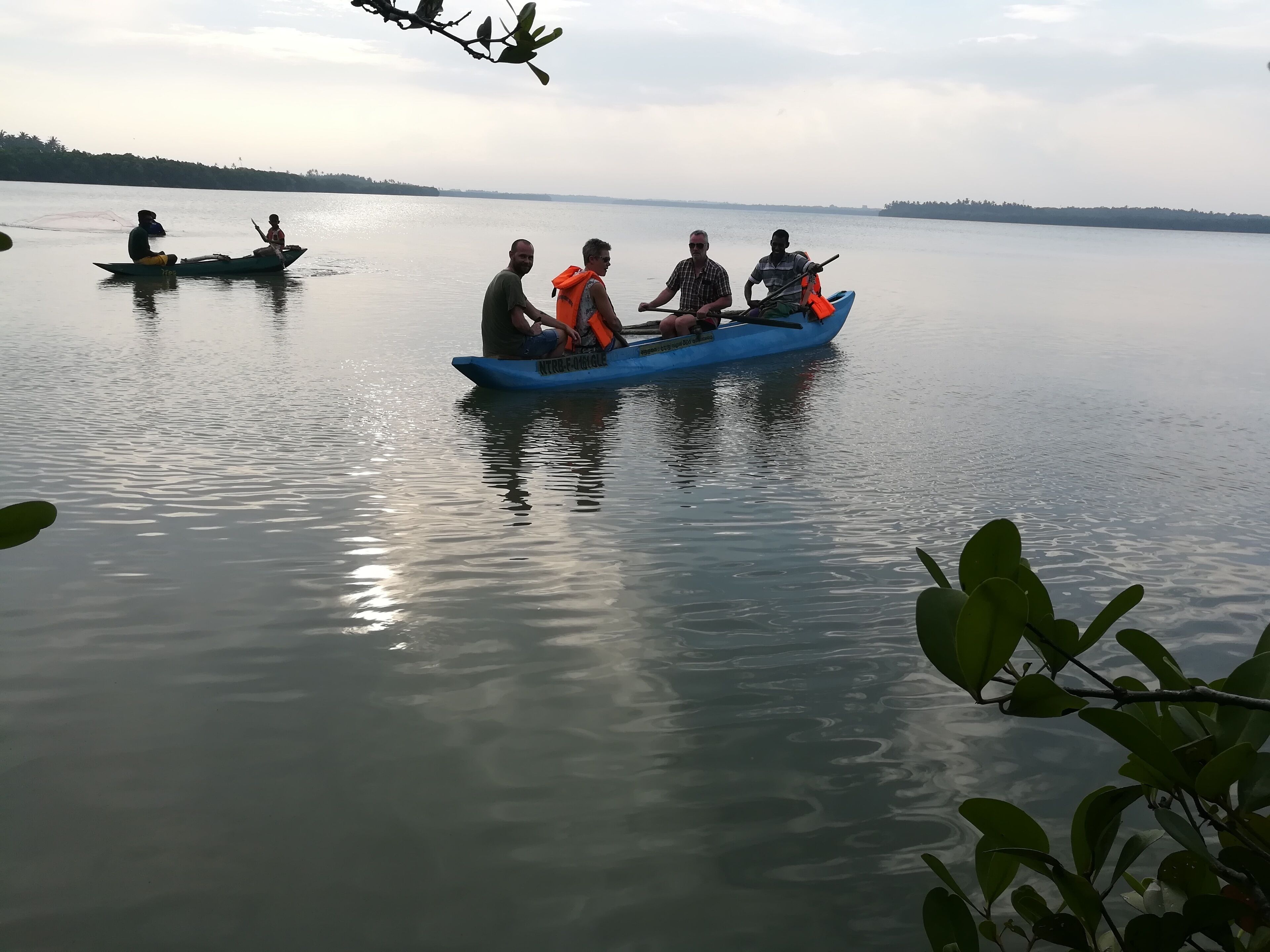 Un grupo de personas en un bote azul sobre un lago tranquilo, con árboles lejanos y un cielo despejado.