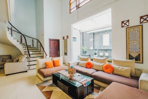 Una sala de estar moderna con una escalera, un conjunto de sofás, una mesa de centro y un ventanal grande.