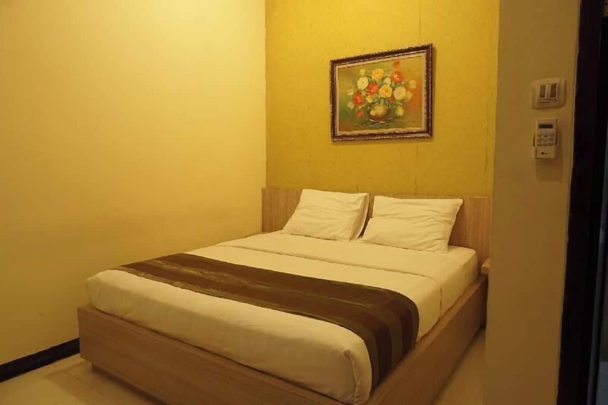 A hotel room with a bed, a painting on the wall, and a thermostat.