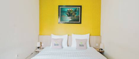 Habitación de hotel con cama, dos almohadas, mesita de noche, lámpara y un cuadro en la pared.