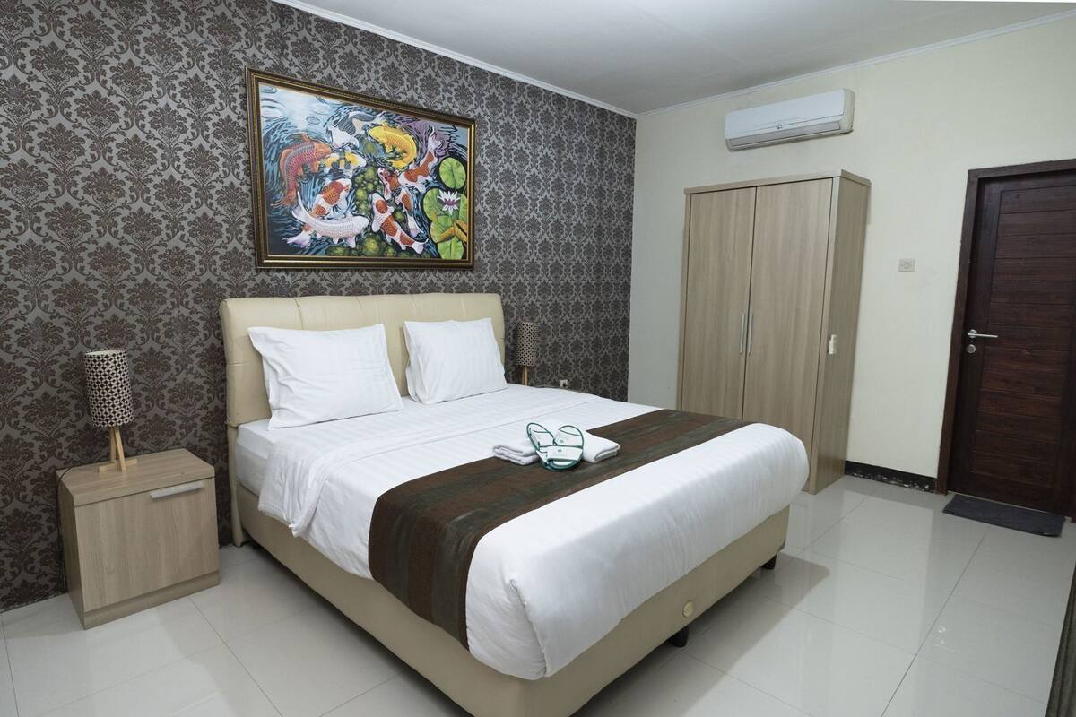 A neatly arranged bedroom with a bed, a nightstand, a wardrobe, and a painting on the wall.