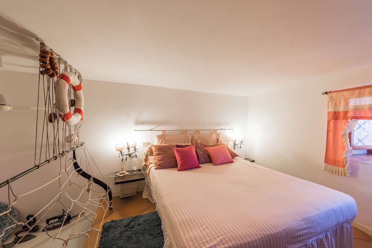 Une chambre à coucher avec un lit, des tables de chevet, un luminaire suspendu et une fenêtre avec des rideaux.