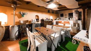 Een gezellig eetgedeelte met houten tafels en stoelen, een hanglamp en een stenen muur.