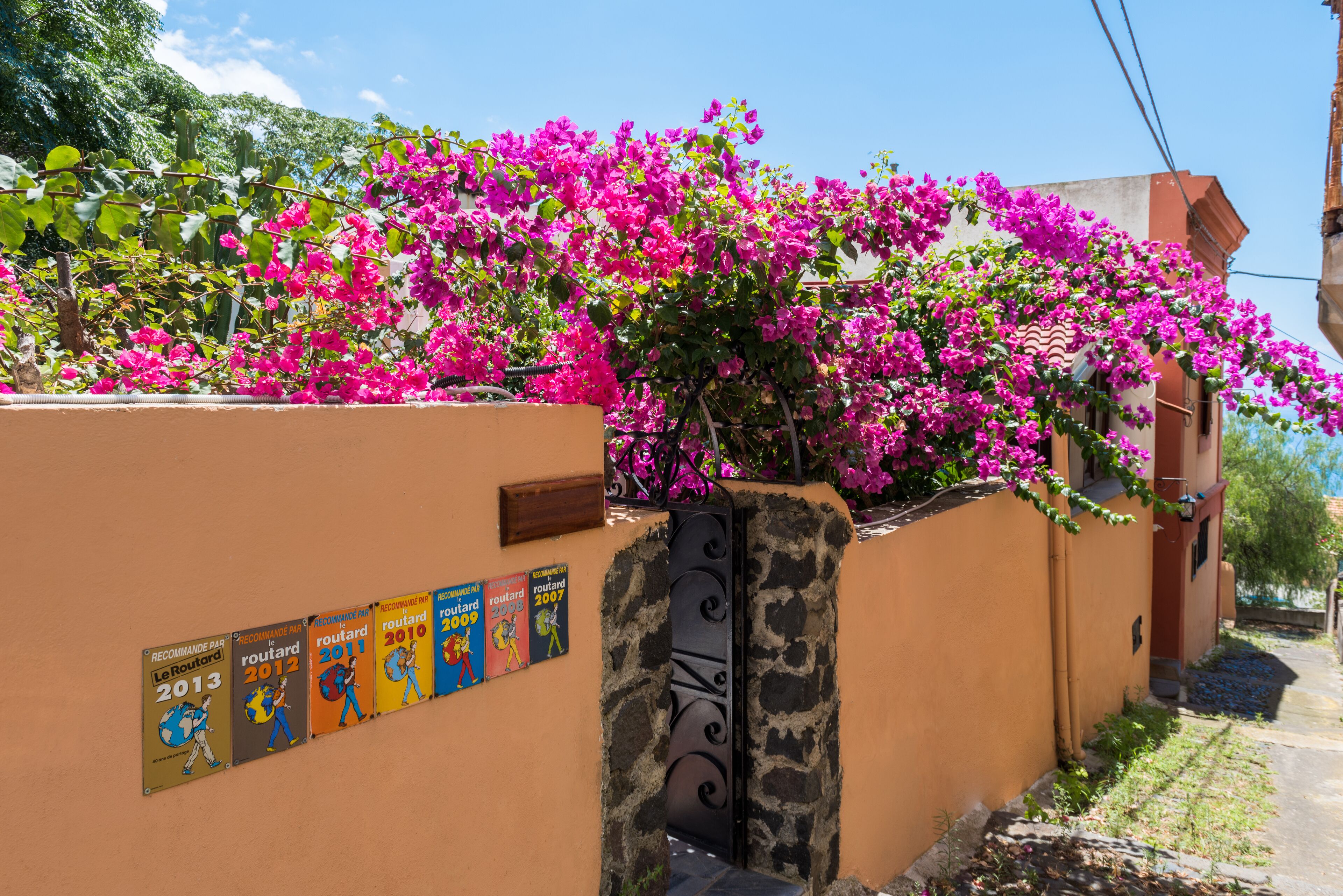 A building with a stone wall and a metal gate, surrounded by vibrant pink bougainvillea flowers.