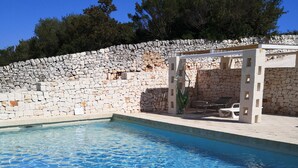 Ein Schwimmbecken mit klarem, blauem Wasser, umgeben von einer Steinmauer und einer Pergola mit einer Hängematte.