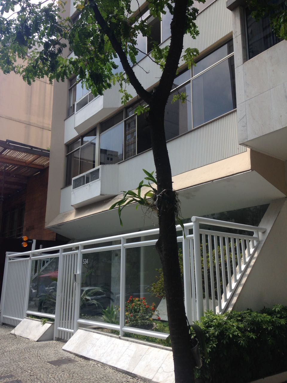 Ein modernes Gebäude mit Balkon, großen Fenstern und einem Baum davor.