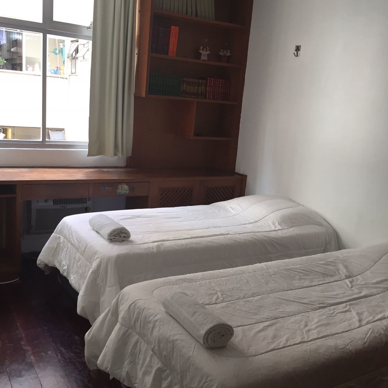 A room with two single beds, a wooden desk, and a window with curtains.