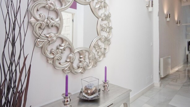 A hallway with a decorative mirror, a small table with two candles, and a vase with dried flowers. - Imperial Deluxe Plaza Mayor (Madrid)