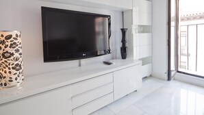 A modern living room with a large flat-screen TV mounted on a white wall, a vase, and a remote control on a white console table. - Imperial Deluxe Plaza Mayor (Madrid)