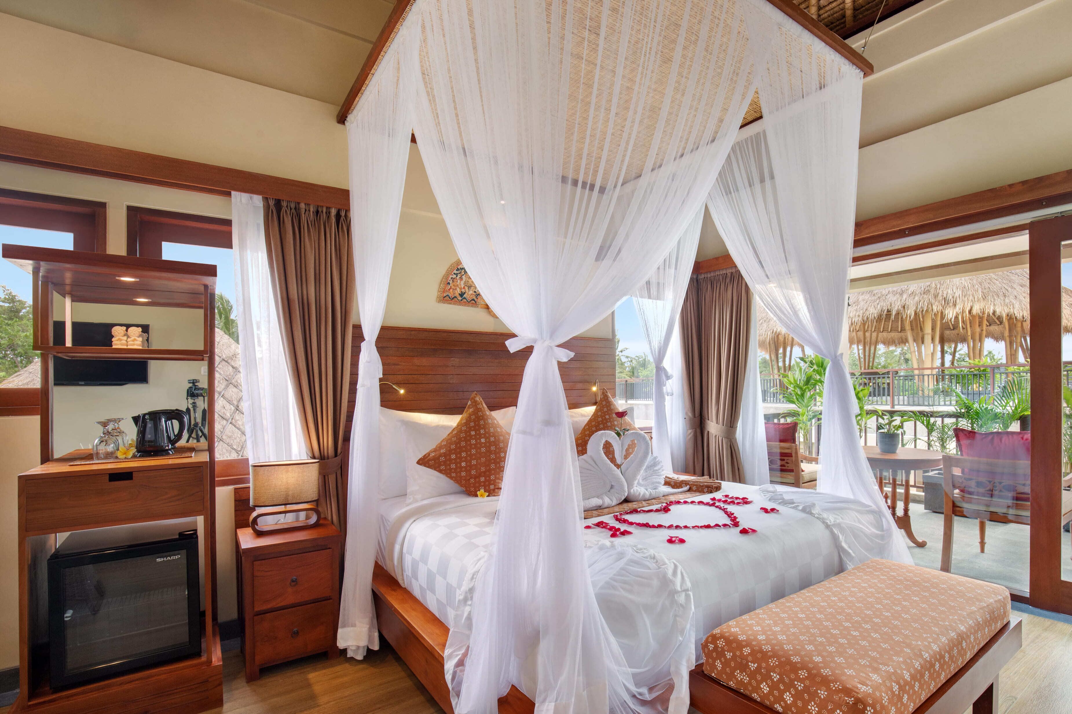 A bedroom with a canopy bed, bedside tables, a TV, and a balcony with outdoor seating.