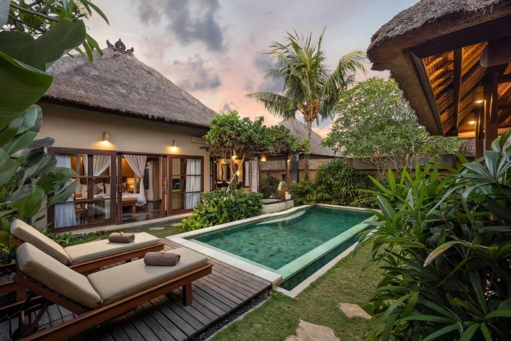 A poolside area with lounge chairs, a thatched-roof structure, and lush greenery.