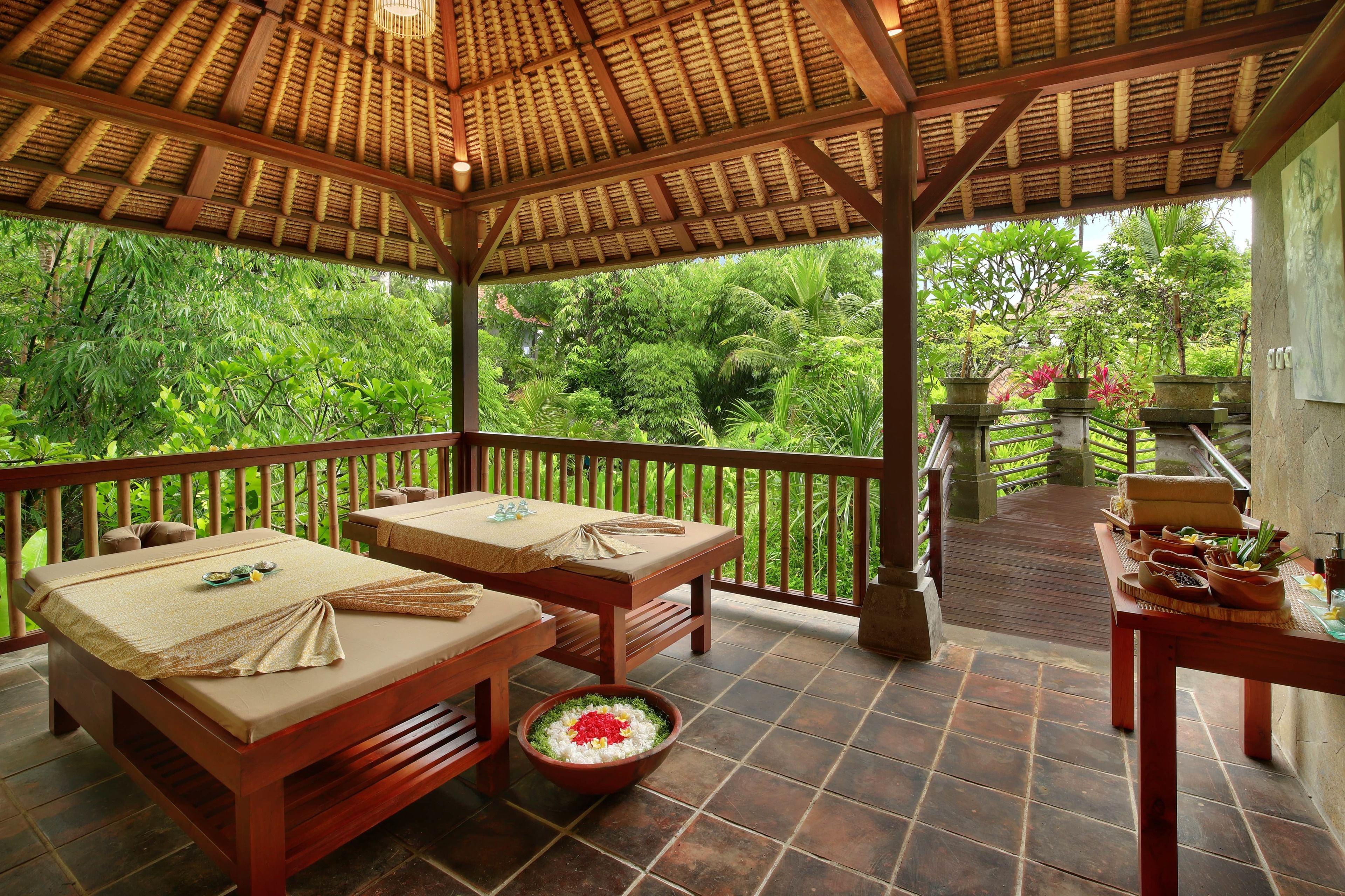 A wooden gazebo with a tiled floor, two massage tables, and a small altar with flowers.