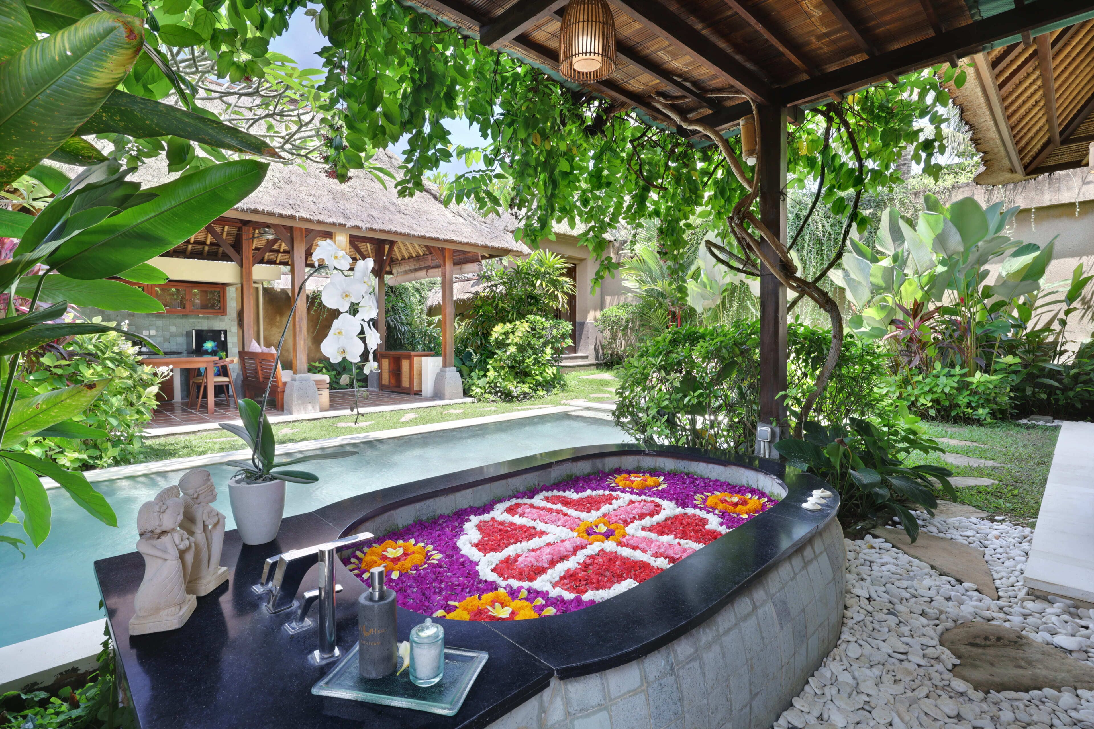 A pool with a flower arrangement, a thatched-roof structure, and lush greenery.