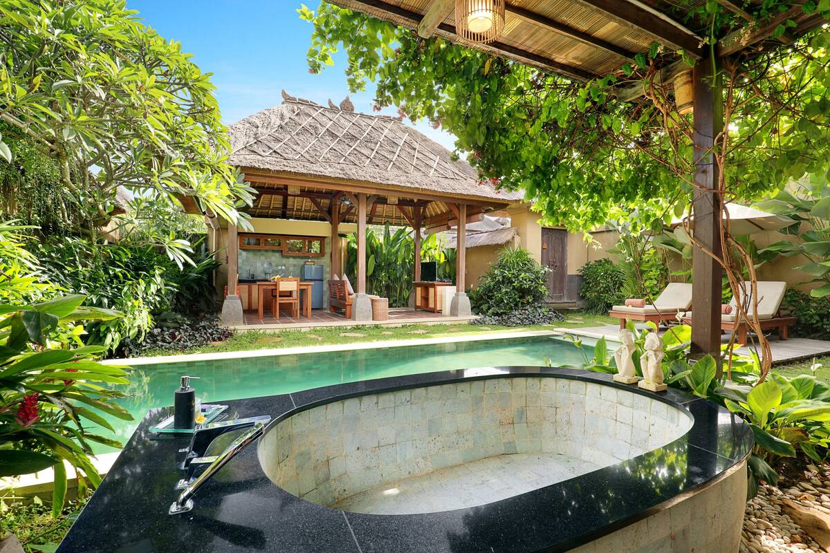Een zwembadgedeelte met een jacuzzi, ligbedden en een overdekte zithoek, omgeven door weelderige begroeiing.