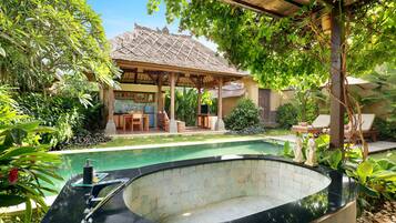 A pool area with a hot tub, lounge chairs, and a covered seating area surrounded by lush greenery.