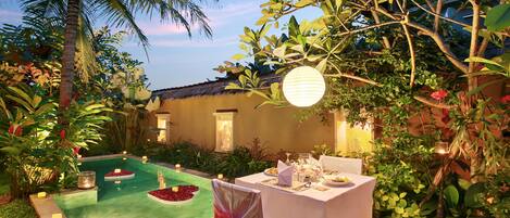An outdoor dining area with a pool, surrounded by lush greenery and palm trees.