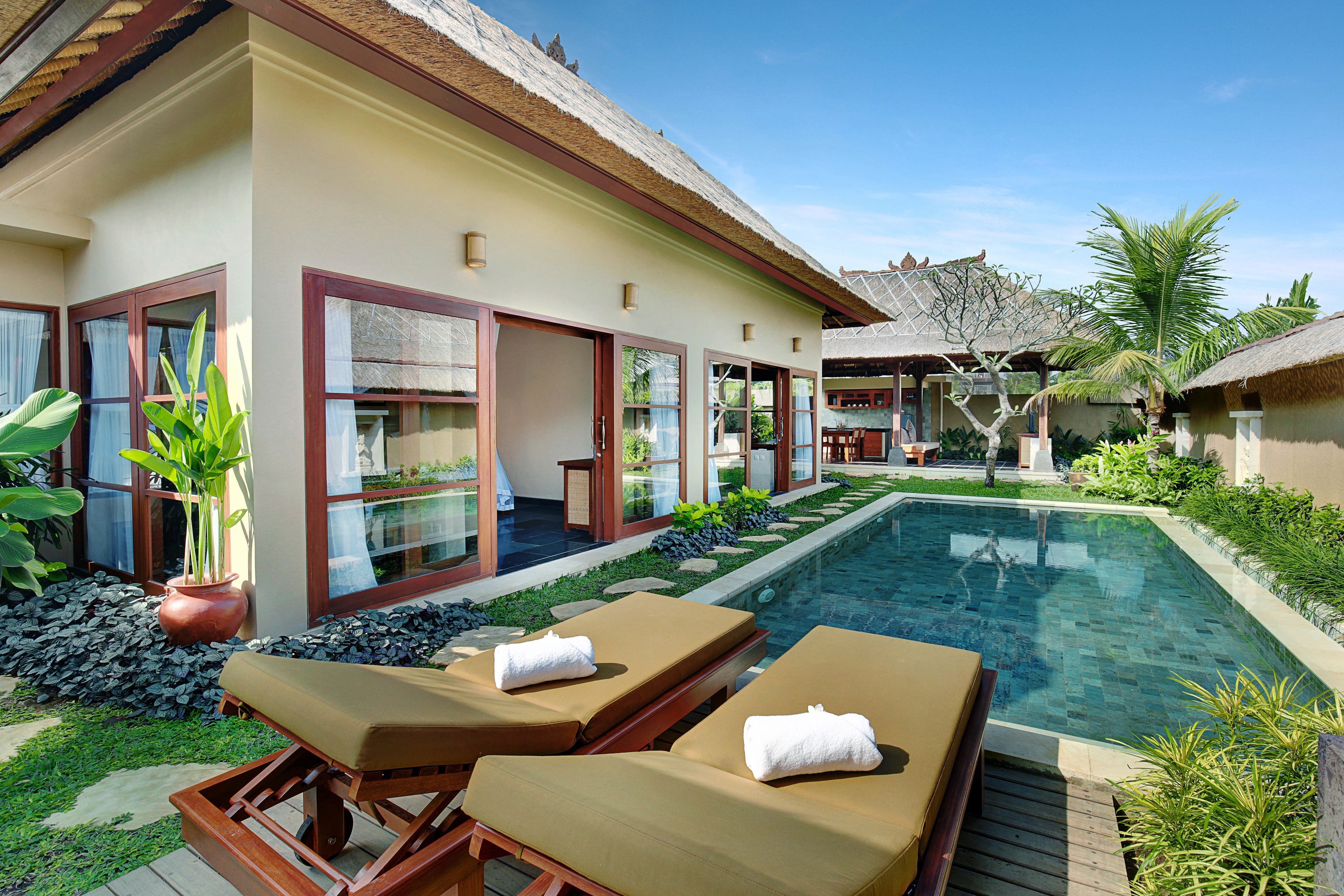 A resort with a swimming pool, lounge chairs, and a thatched-roof building.