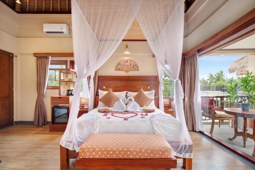 A bedroom with a canopy bed, a bedside table, a small desk, and a view of the outdoors.