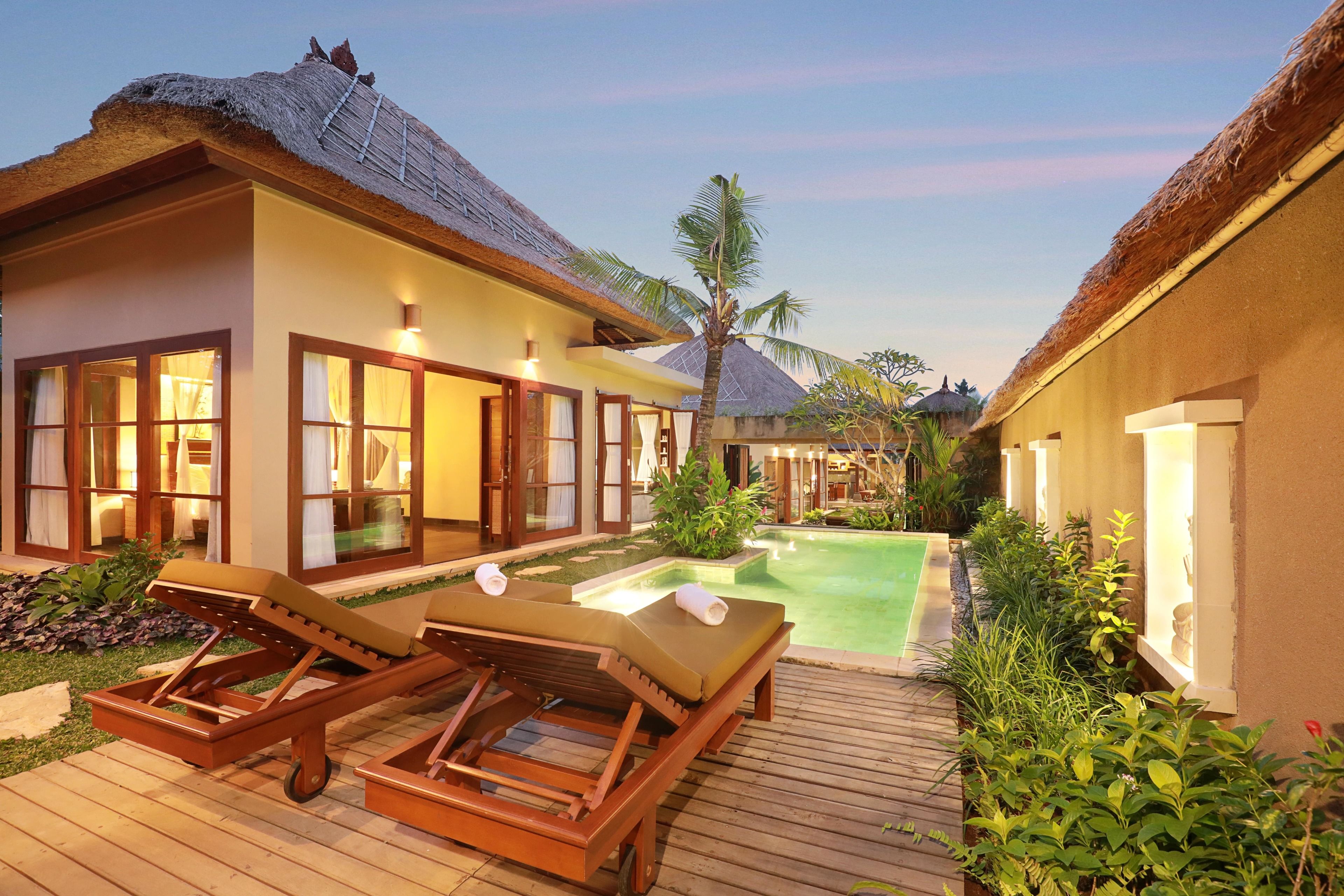 Resort com villas de telhado de palha, piscina e espreguiçadeiras de madeira.
