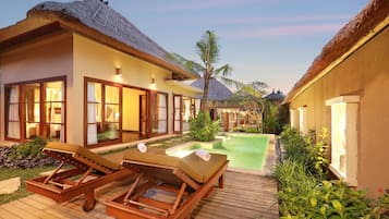 Resort com villas de telhado de palha, piscina e espreguiçadeiras de madeira.