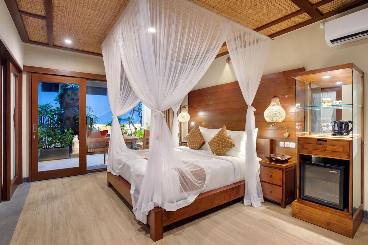 Een ruime slaapkamer met een houten bed, een witte hemelbed en een glazen deur naar een balkon.