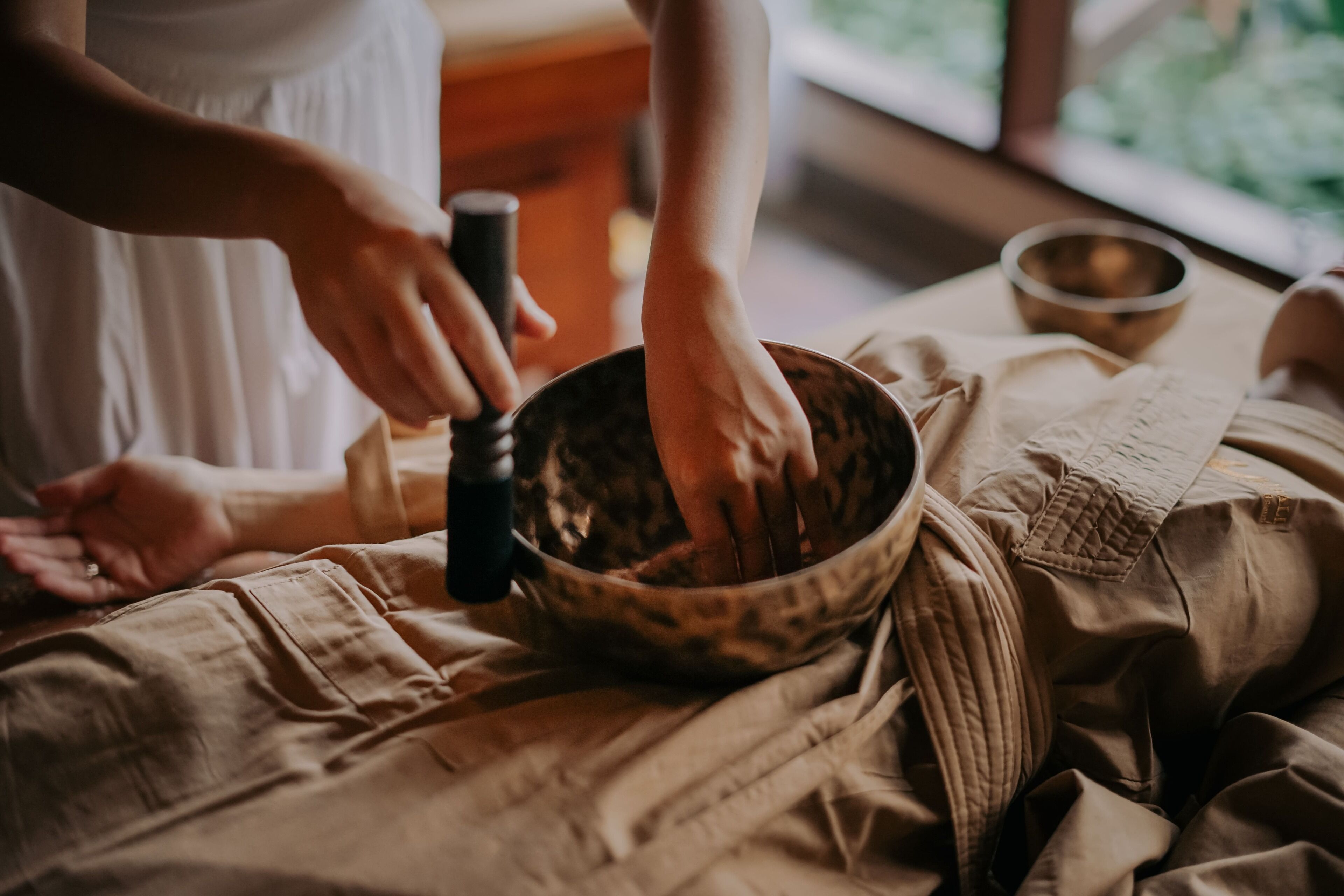 Una persona con un vestido blanco usando un cuenco de madera y un utensilio con mango negro, probablemente para un ritual o ceremonia.
