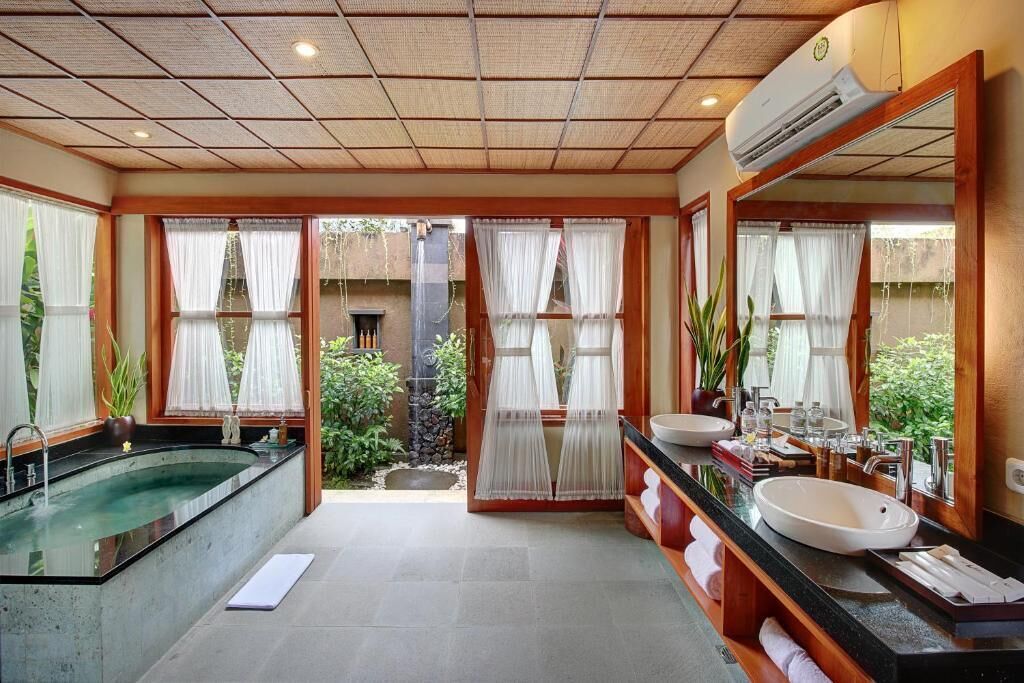 Casa de banho com banheira, duas pias, um espelho grande e vista para o verde lá fora.