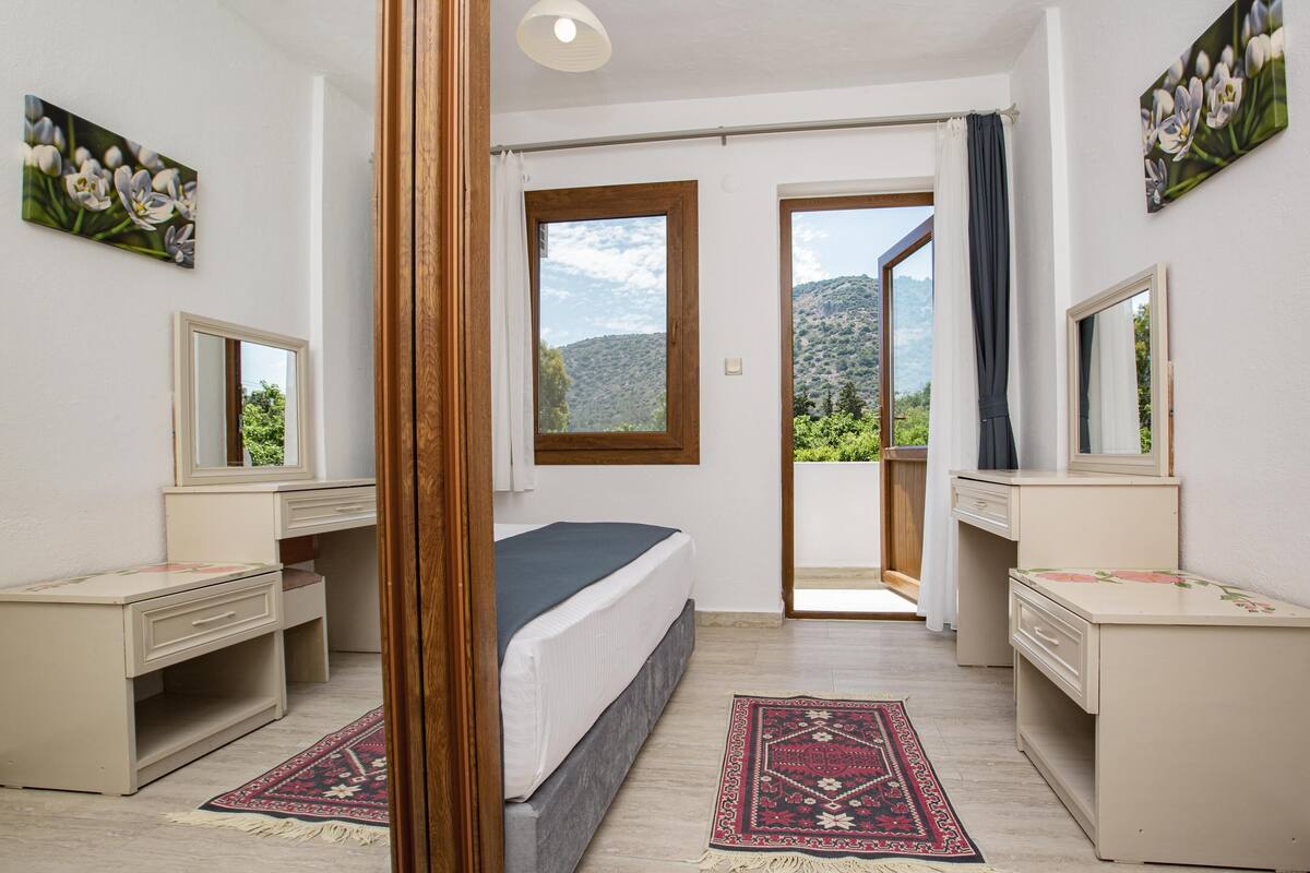 Ein Schlafzimmer mit einem Bett, zwei Schreibtischen, einem Spiegel und Blick auf eine Berglandschaft.