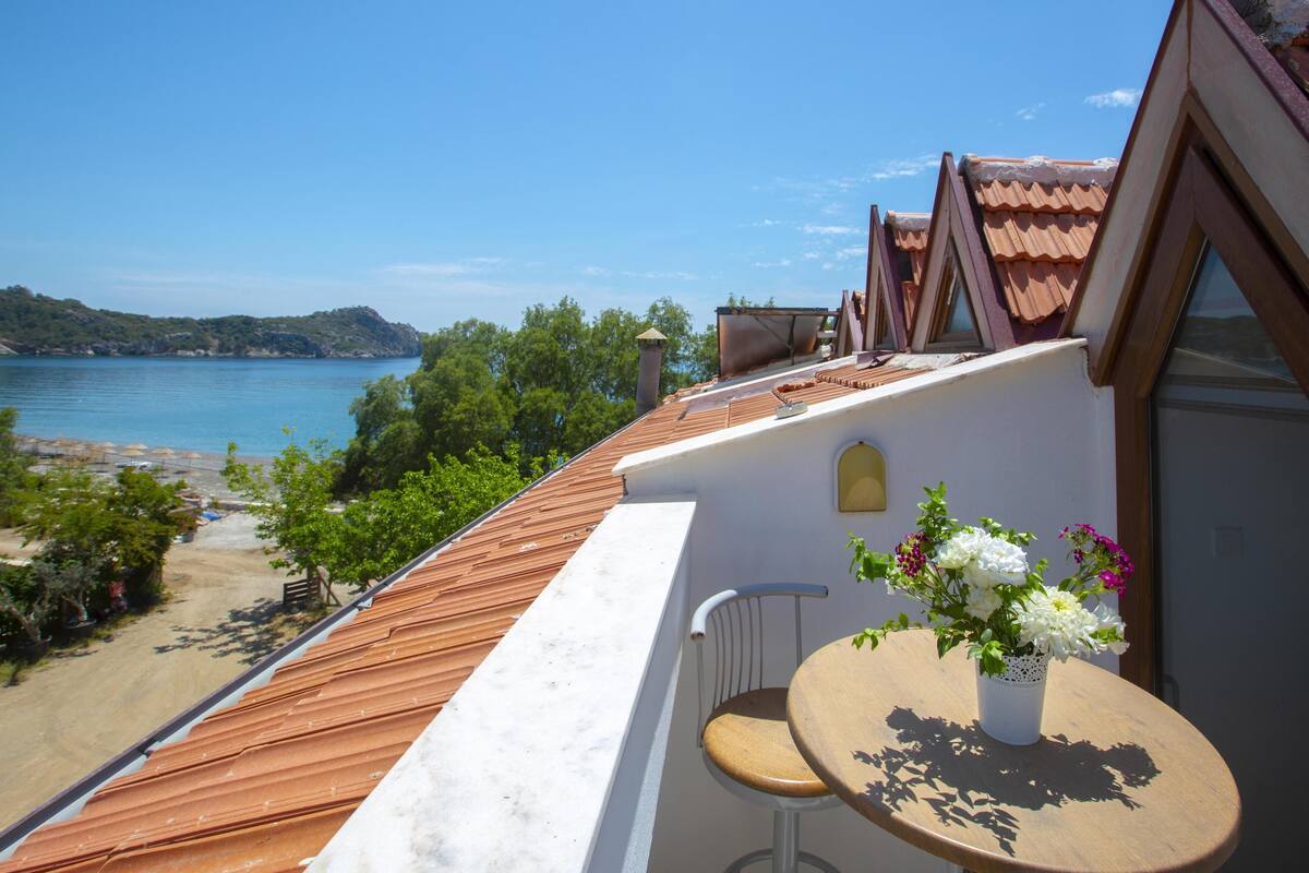Ein Balkon mit Meerblick, ein Tisch mit Blumen in einer Vase und ein Stuhl.