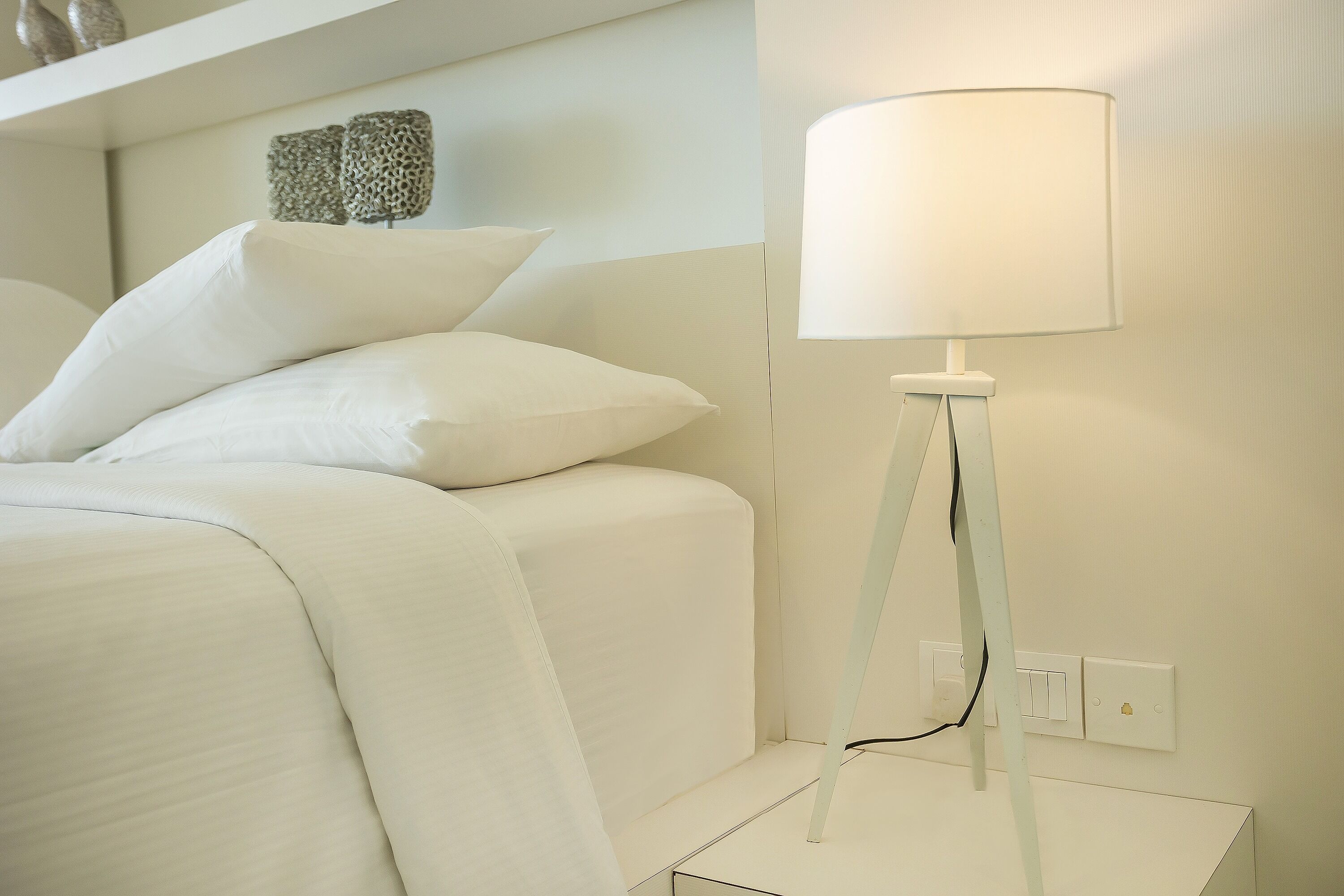Ein ordentlich bezogenes Bett mit weißen Leinen und einer weißen Nachttischlampe.