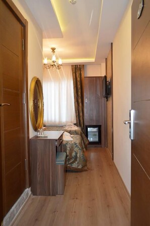 A hotel room with a wooden floor, a bed with patterned bedding, a bedside table, a mirror, and a television. - Grand Gross Hotel (Istanbul)