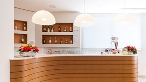 Ein Empfangsbereich mit einer gebogenen Holztheke, Regalen mit Spirituosenflaschen und zwei Pendelleuchten.