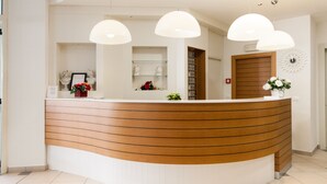 Ein Empfangstresen mit geschwungener Holzoptik, weißen Wänden und drei Pendelleuchten.