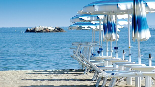 Ein Strand mit weißen Liegestühlen und blau-weiß gestreiften Sonnenschirmen.