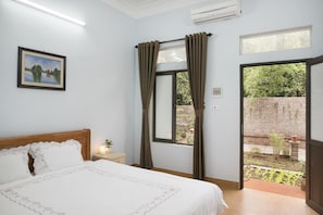 A bedroom with a bed, a nightstand, a window with curtains, and a view of an outdoor garden. - Tam Coc Craft Homestay (Hoa Lu)