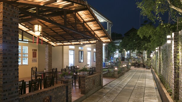 A covered outdoor seating area with brick walls and tiled flooring, featuring tables and chairs. - Tam Coc Craft Homestay (Nam Hoa Lu)