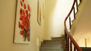 A staircase with a wooden handrail and a painting of red flowers on the wall. - Tam Coc Craft Homestay (Nam Hoa Lu)
