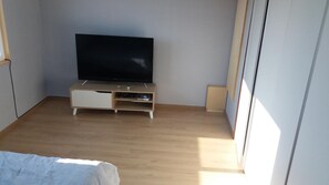A bedroom with a bed, a TV on a wooden stand, and a window.