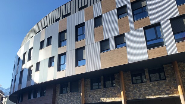 A multi-story building with a modern architectural design, featuring a combination of brick and metal panel facades, multiple windows, and a visible entrance.