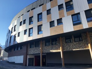 Ein mehrgeschossiges Gebäude mit moderner Architektur, das Ziegel- und Metallfassaden, zahlreiche Fenster und einen gut sichtbaren Eingang kombiniert.